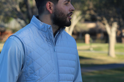 Man wearing a light gray quilted vest outdoors with trees in the background