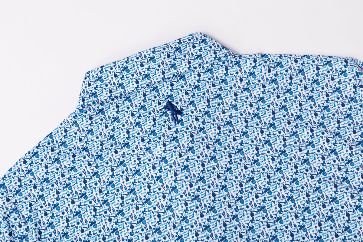 A close-up of a blue and white patterned fabric, likely a shirt or scarf, featuring a small embroidered dark blue logo on the collar, set against a plain white background.