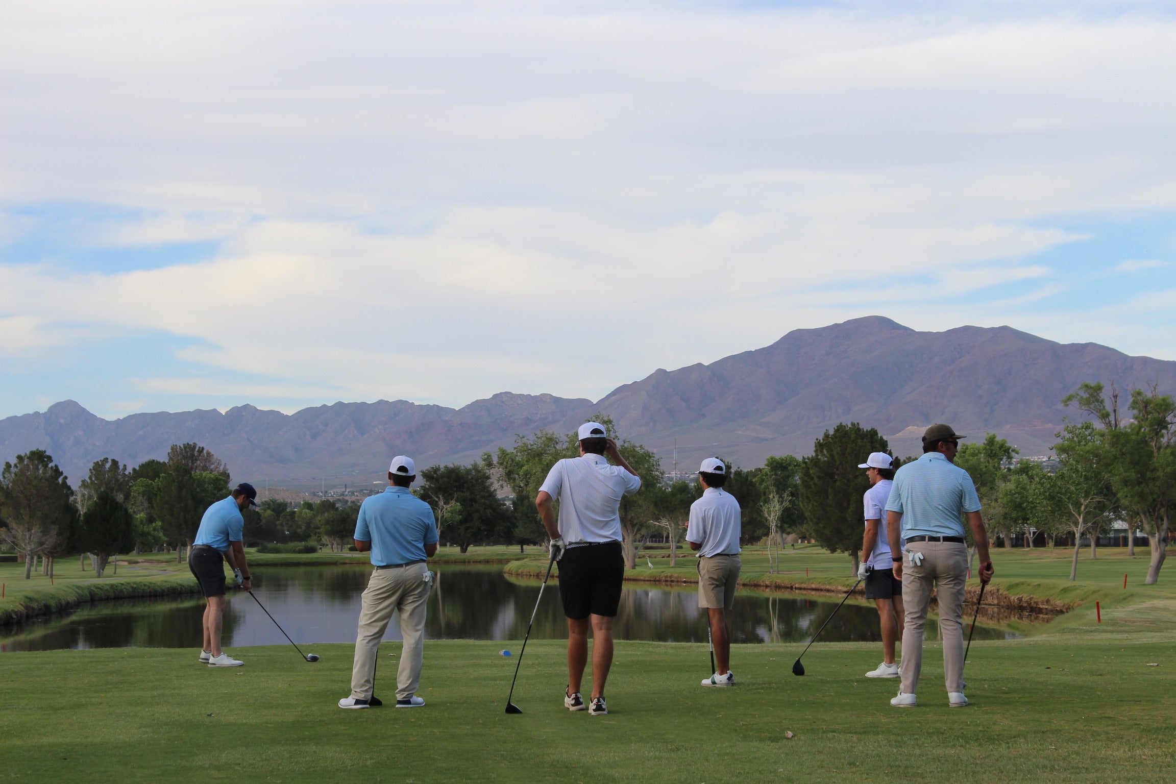 Group of golfers teeing off over lake
