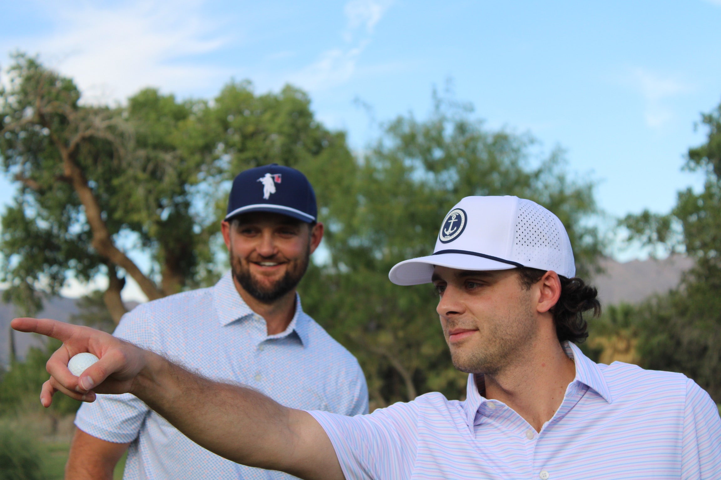 Two golfers pointing while wearing hats