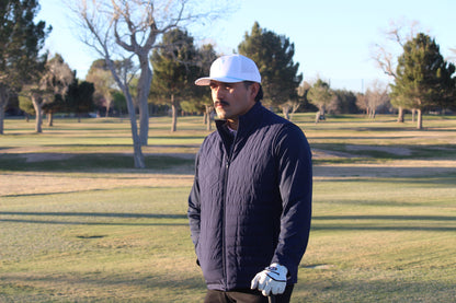 Man in a navy vest and white cap standing on a golf course