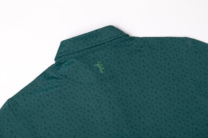 A close-up of a dark green collared shirt with a subtle repeating geometric pattern and a small green embroidered logo on the upper back, shown against a plain white background.